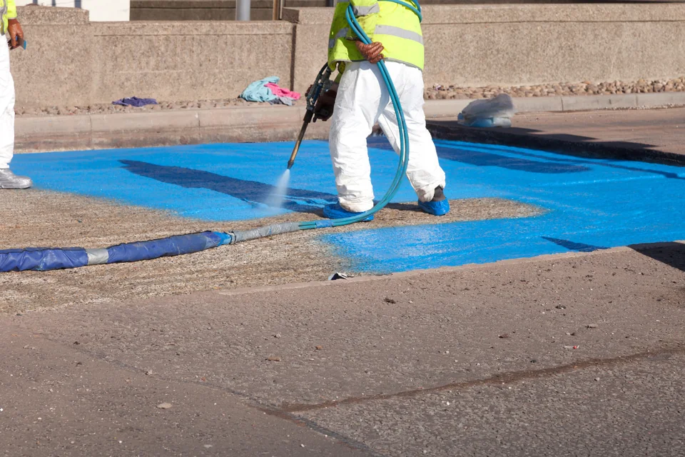 Worker applying flooring system with a spray machine